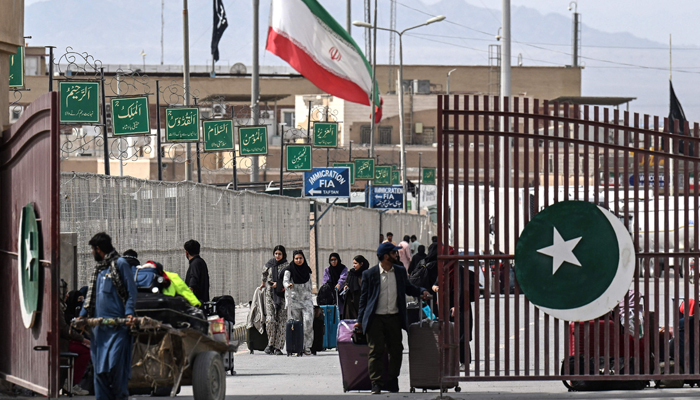 Pakistani nationals walk across the Pakistan-Iran border after returning from Iran as an Iranian national flag (centre) flies at half-mast at Taftan, Balochistan province on March 2, 2026 after the death of Irans supreme leader Ayatollah Ali Khamenei amid US-Israel strikes. — AFP
