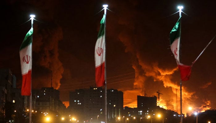 Iranian flags fly high as fire rages in the background following an Israeli attack on Sharan Oil Depot. — Reuters/File