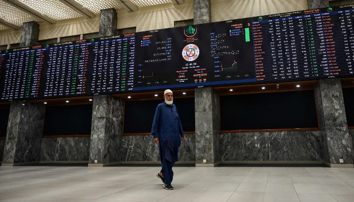 A stockbroker walks past a digital board showing share prices at the Pakistan Stock Exchange (PSX) in Karachi on March 10, 2026. — AFP