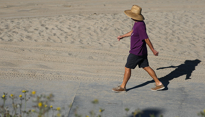 A person wears a hat for shade under the morning sun while walking along The Strand in Redondo Beach, California on March 20, 2026, during a heat wave. — AFP