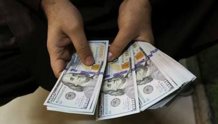 A trader counts US dollar banknotes at a currency exchange booth in Peshawar. — Reuters/File
