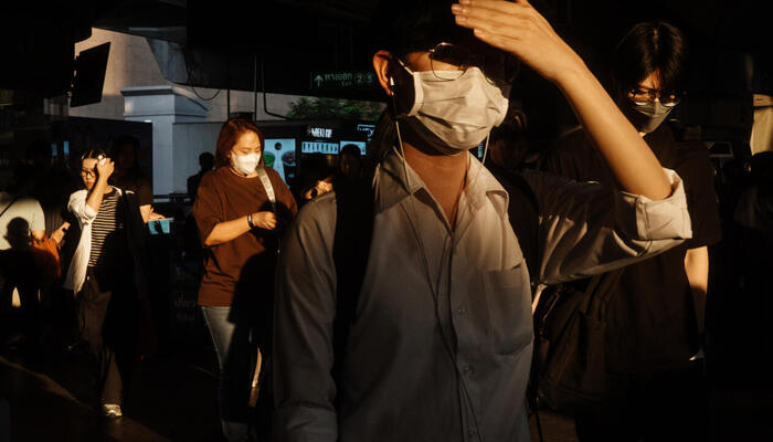 A man covers his face with his hand from the sun while people walk on a street in Indonesia. — AFP