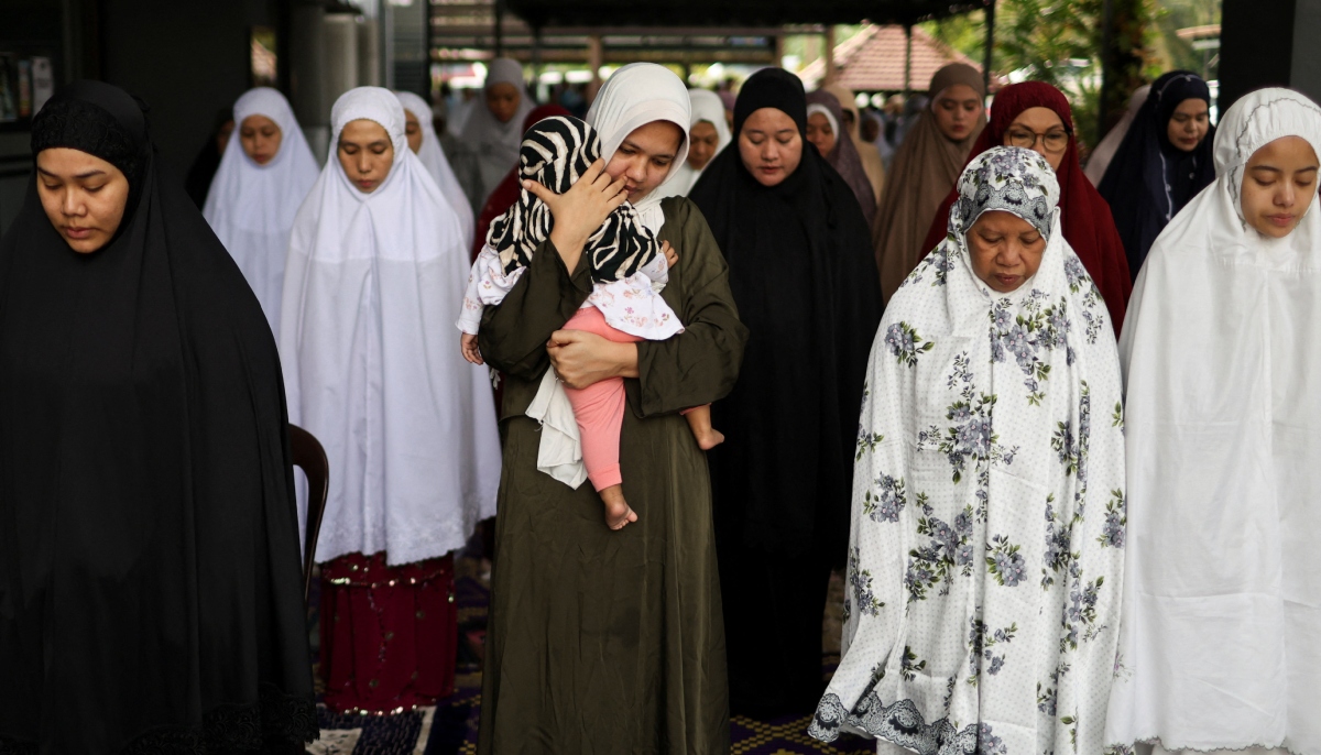 A Muslim woman carries a toddler as she performs Eid ul Adha mass prayers at a mosque in Ampang, Malaysia, May 27, 2026. — Reuters