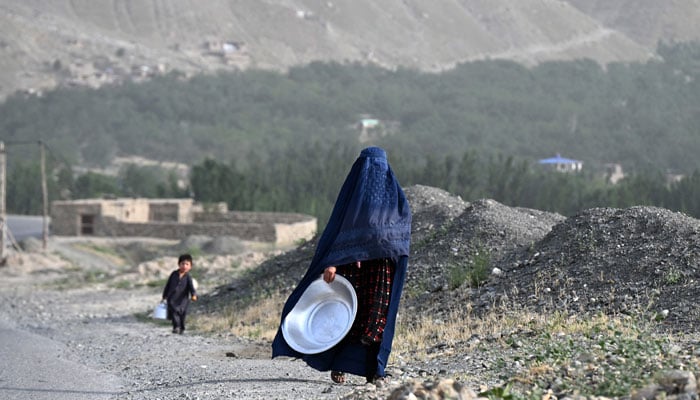 An Afghan burqa-clad woman carrying a large utensil walks along a street in Argo district of Afghanistans Badakhshan province on June 10, 2026.— AFP