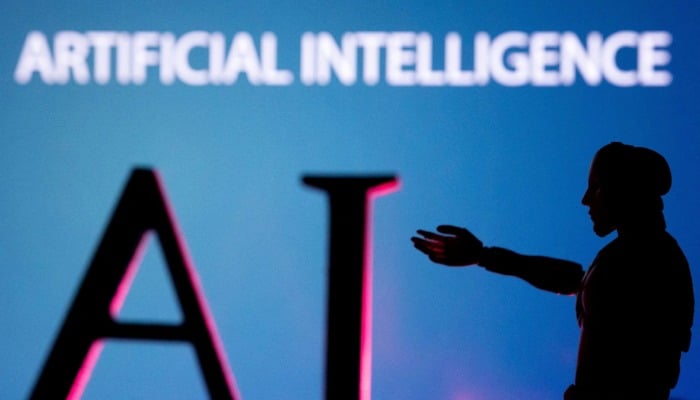 A robot silhouette is seen next to the words artificial intelligence written on a wall. — Reuters