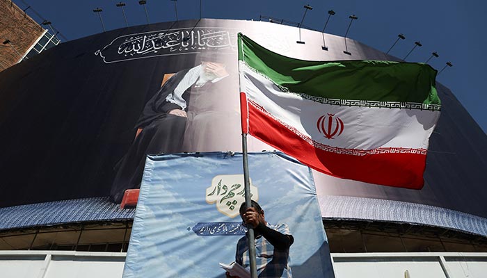A man holds an Iranian flag on a street, after U.S. and Iranian officials said they had reached a deal to end their war and reopen the Strait of Hormuz, in Tehran, Iran, June 15, 2026. — Reuters