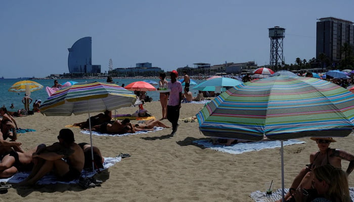 A man sells drinks for tourists and locals as they enjoy the Barceloneta beach as temperatures rise, during a heatwave affecting a large part of Spain, in Barcelona, Spain, June 21, 2026.  — Reuters
