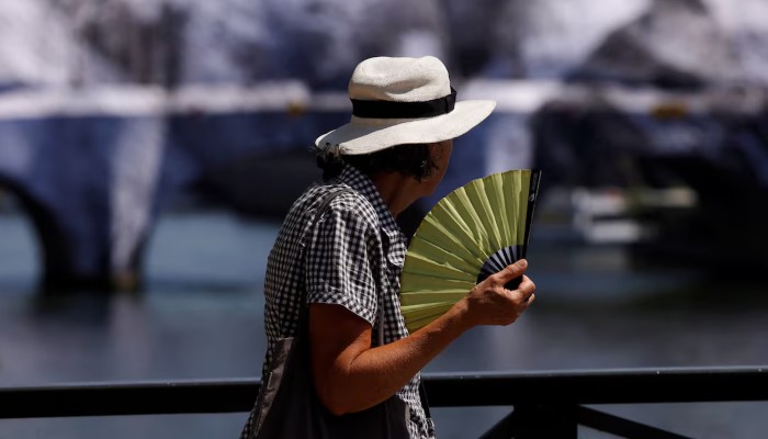 A person wearing a hat and holding a hand fan walks on the Pont des Arts bridge over the River Seine in Paris as temperatures rise during a heatwave affecting a large part of France, June 22, 2026. — Reuters