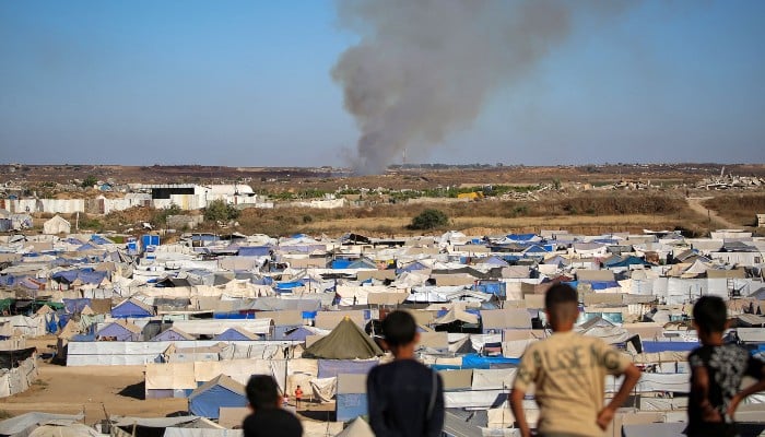 Children watch from atop a promontory overlooking shelters for people displaced by war, as smoke billows in the background near the Nuseirat camp for Palestinian refugees in the central Gaza Strip on June 19, 2026. — AFP