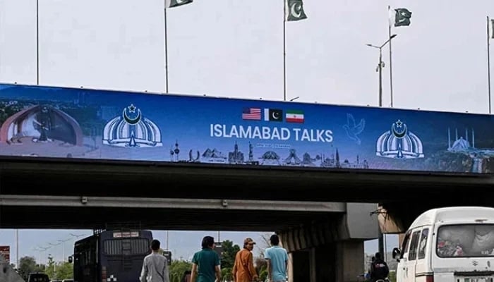 Boys walk under a digital screen displaying news of US-Iran peace talks along a road in Islamabad on April 10, 2026. — AFP