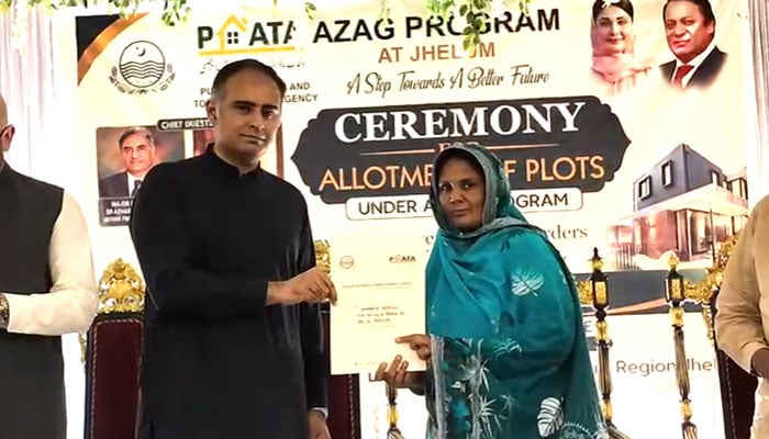 Minister of State for Finance and Railways Bilal Azhar Kiyani hands over an allotment letter for a plot to a deserving woman in Jhelum on July 4, 2026. — Geo News