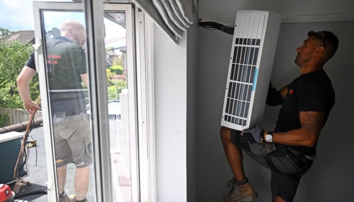 Engineers install an air conditioning unit at a residential home in Croydon, south London, Britain, on July 1, 2026. — AFP