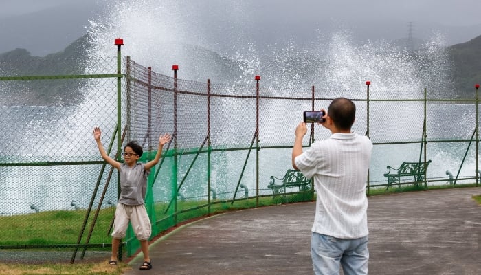 A man takes a photograph of a child posing as waves crash against the shoreline as Typhoon Bavi approaches in Keelung, Taiwan, July 10, 2026. — Reuters
