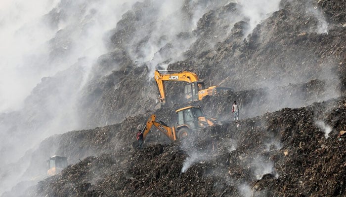 Picture shows an excavator tries to contain the fire as smoke billows from burning garbage at landfill site. — Reuters