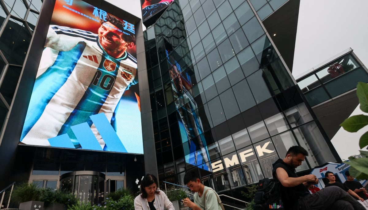 People sit on a bench in front of a giant advertisement screen featuring a portrait of Argentinas soccer player Lionel Messi, in Beijing, China on July 16, 2026. — Reuters