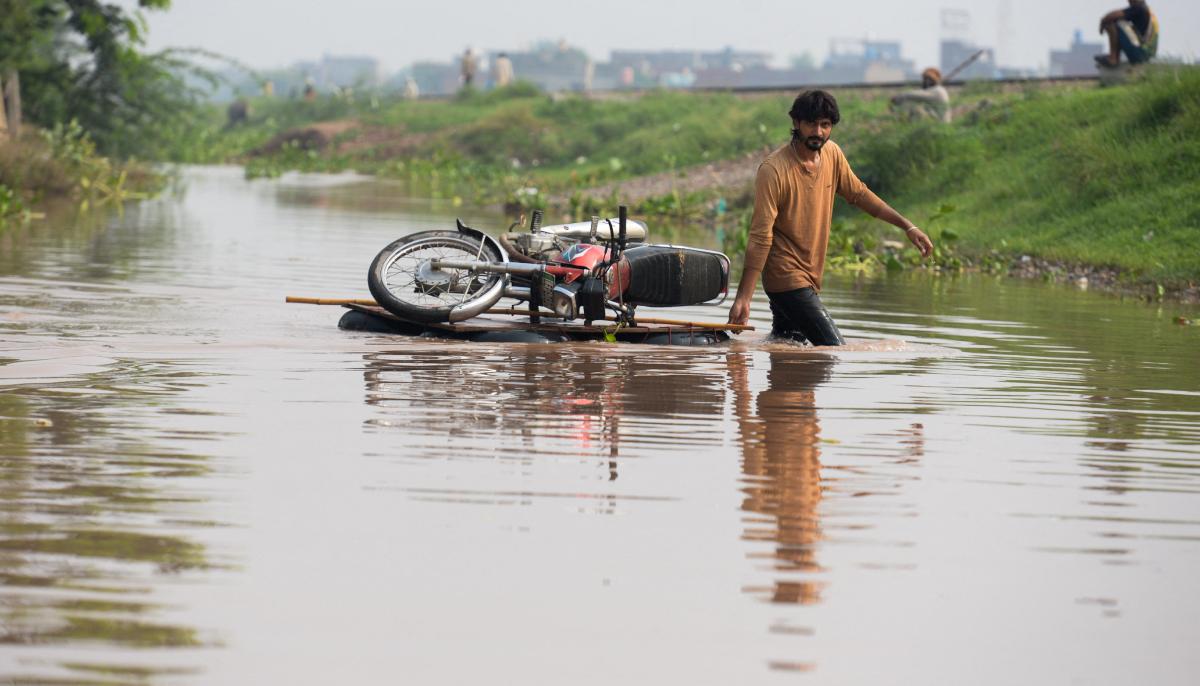 A man pulls his motorcycle across a wooden plank through floodwaters following monsoon rains in Ferozwala, on July 30, 2026. — Reuters