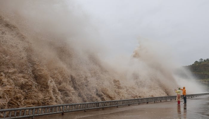 People stand next to huge waves crashing on a waterfront as Typhoon Dolphin approaches, in Sanmen County, Taizhou, Zhejiang Province, China, August 8, 2026. — Reuters