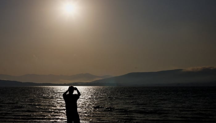 A tourist photographs the sun with his mobile phone at Arija beach, Spain, August 11, 2026. — Reuters