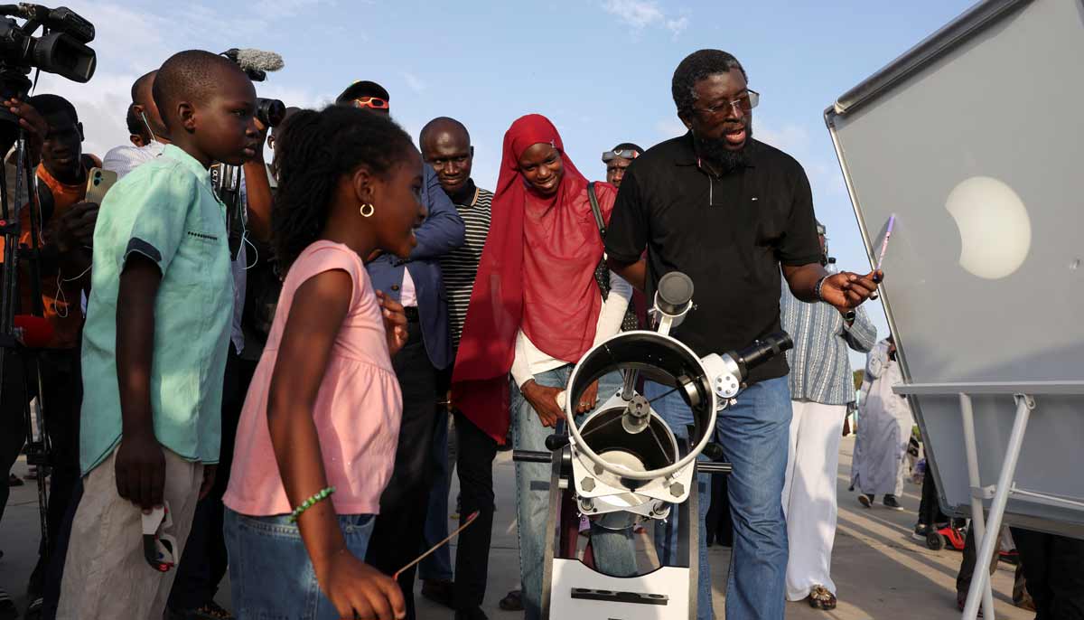 A man projects an image of the sun onto a screen via a telescope with a solar filter as people observe, in Dakar, Senegal, August 12, 2026. — Reuters