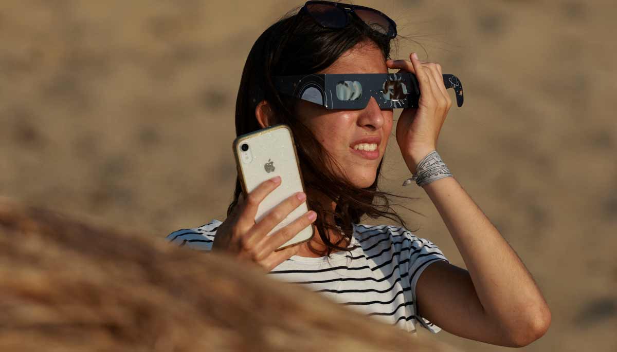 A woman watches a partial solar eclipse through protective glasses from the Dune of Pilat in La Teste-de-Buch near Arcachon, France, August 12, 2026.— Reuters