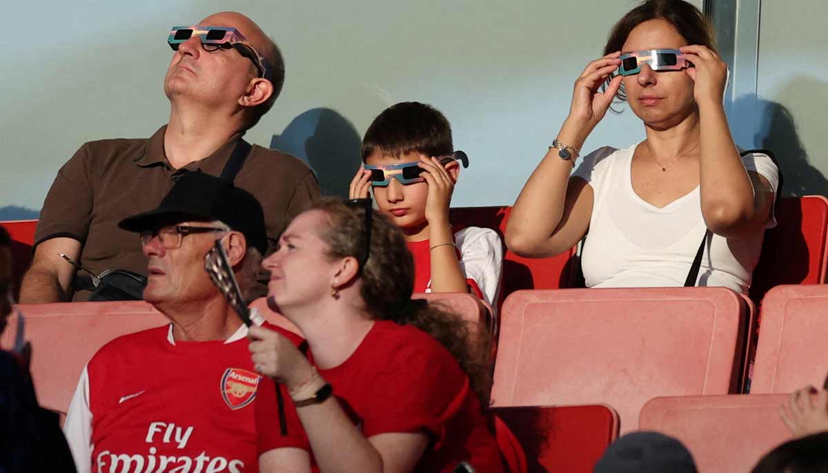 Arsenal fans watch the solar eclipse through protective glasses in the stands before the match. — Reuters
