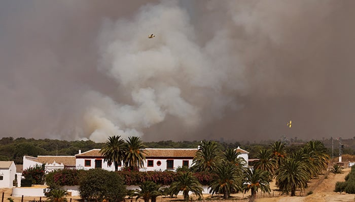 Firefighting planes fly as smoke rises from a wildfire, in Aznalcollar, Spain, August 13, 2026. — Reuters