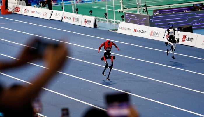 Spectators use smartphones as they watch humanoid robots compete during a 100m large-sized group preliminary race, following the opening ceremony of the 2026 World Humanoid Robot Games, at the National Speed Skating Oval, in Beijing, China, August 22, 2026. — Reuters