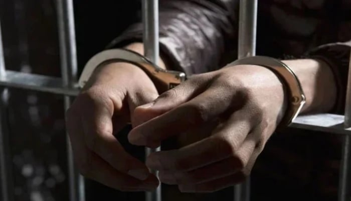 A representational image of a handcuffed man standing behind bars. — APP/File