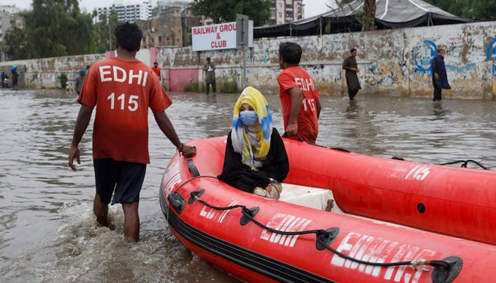 A woman sits in a rubber boat as volunteers pull through a flooded road during the monsoon season in Karachi on July 9, 2022. — Reuters